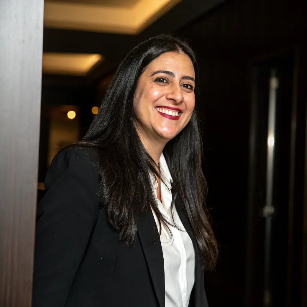 Rubini is a woman with long, wavy brown hair and a professional demeanor. She has a friendly face and often wears a blazer.