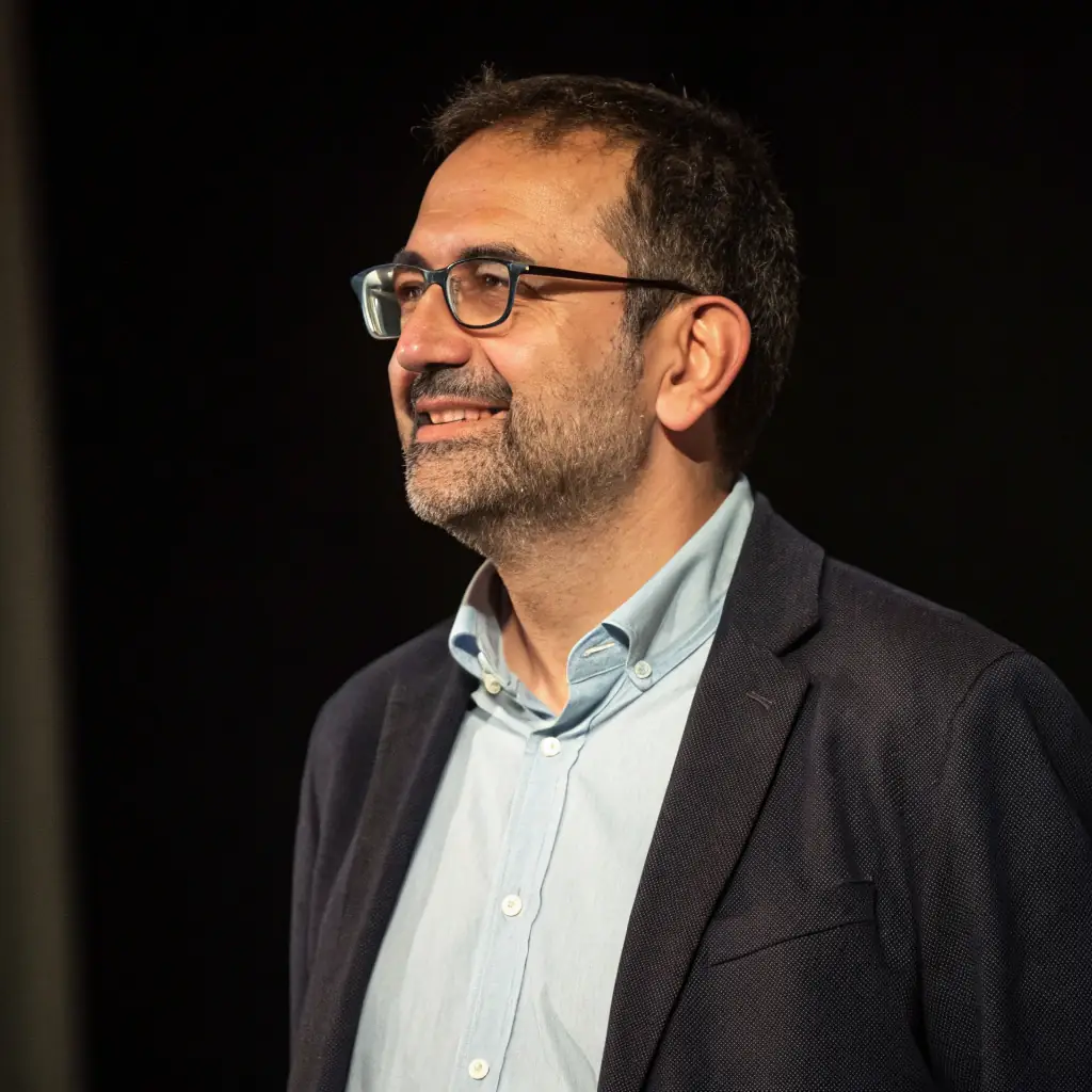 Anthony is a middle-aged man with short, dark hair and a neatly trimmed beard. He wears glasses and has a warm, approachable smile.