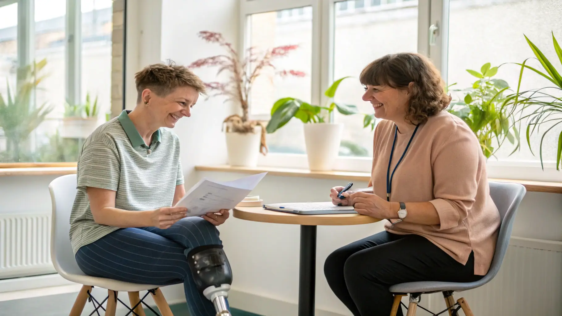A support worker interacting with a participant, both smiling, while the support worker is wearing smart glasses and using voice commands to log information. The setting is a bright and comfortable home environment.