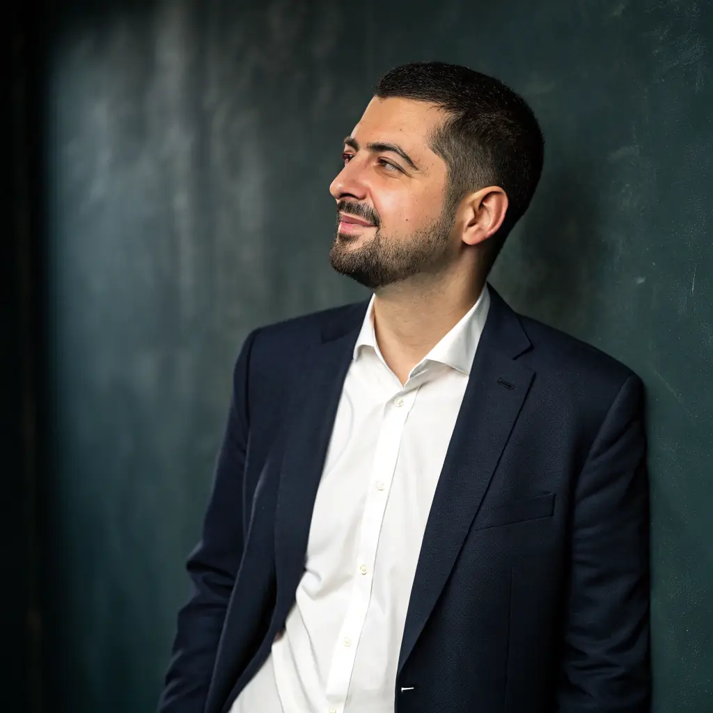 A confident man with a clean-shaven face and short dark hair, wearing a professional business attire.
