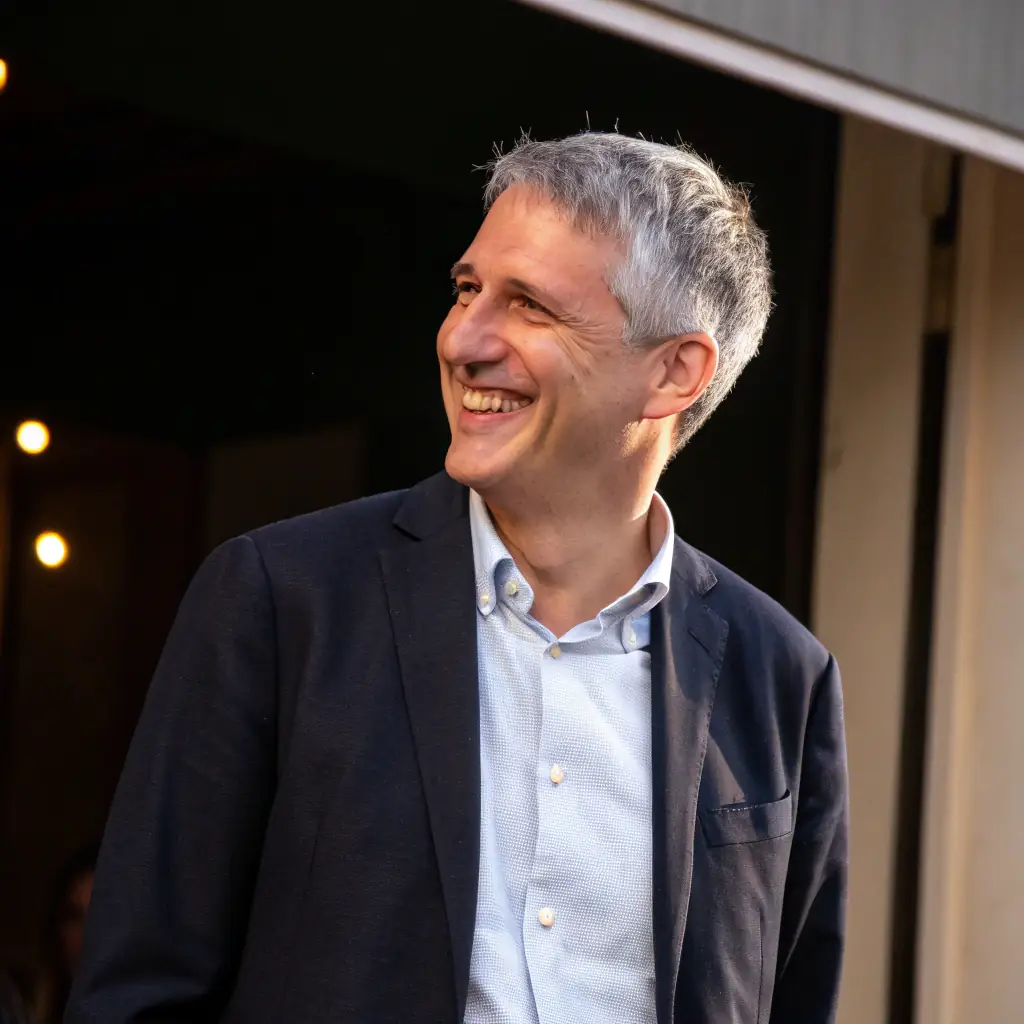 Thomas is a man with graying hair and a kind face, wearing a tweed jacket and a tie.