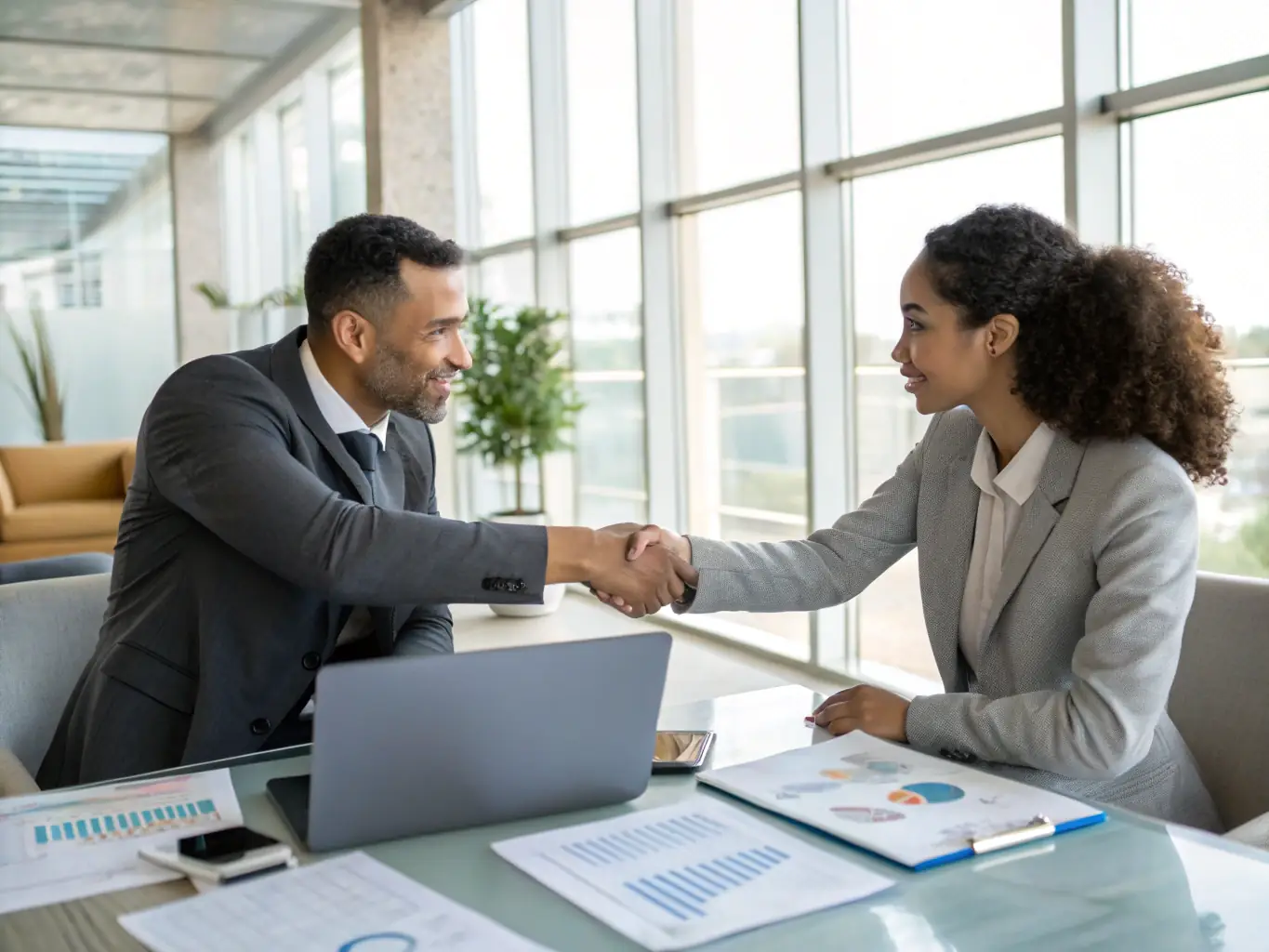 Two people shaking hands over a contract on a desk, symbolizing a secure and professional agreement.
