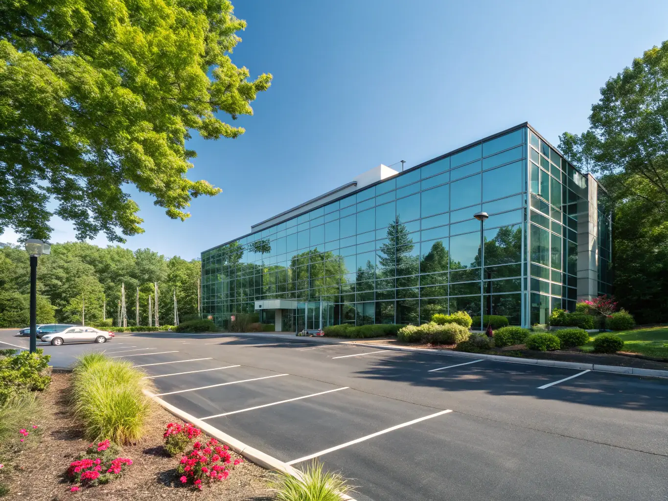 A modern commercial building with glass facade and a parking lot in front of it.