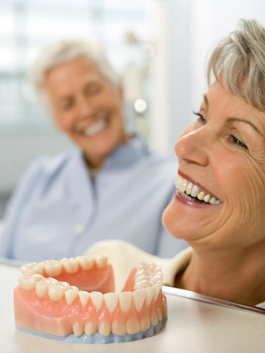 Close-up shot of a complete set of conventional dentures, highlighting the gum-colored acrylic base and natural-looking teeth, placed on a clean, white background in a dental clinic setting.