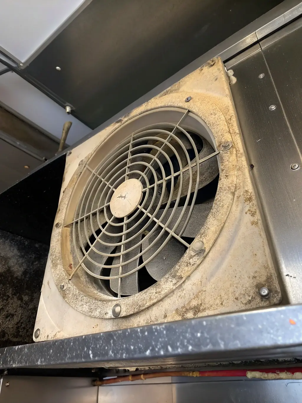 A before-and-after shot of an exhaust fan blade, showing heavy buildup on one side and a clean, shiny surface on the other, highlighting the effectiveness of the fan blade cleaning service.