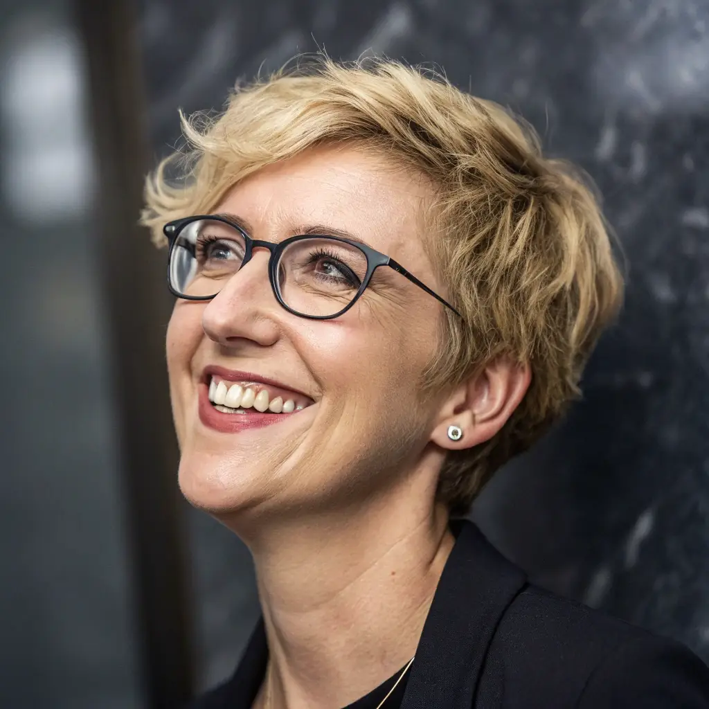 Alice has short blonde hair, wears glasses, and has a warm, approachable smile.