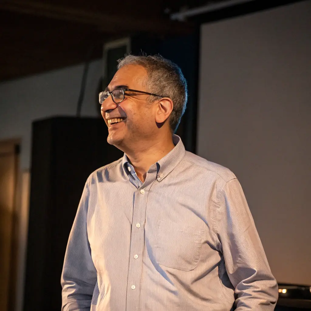 Antoine is a meticulous man with glasses and neatly combed hair, wearing a button-down shirt.