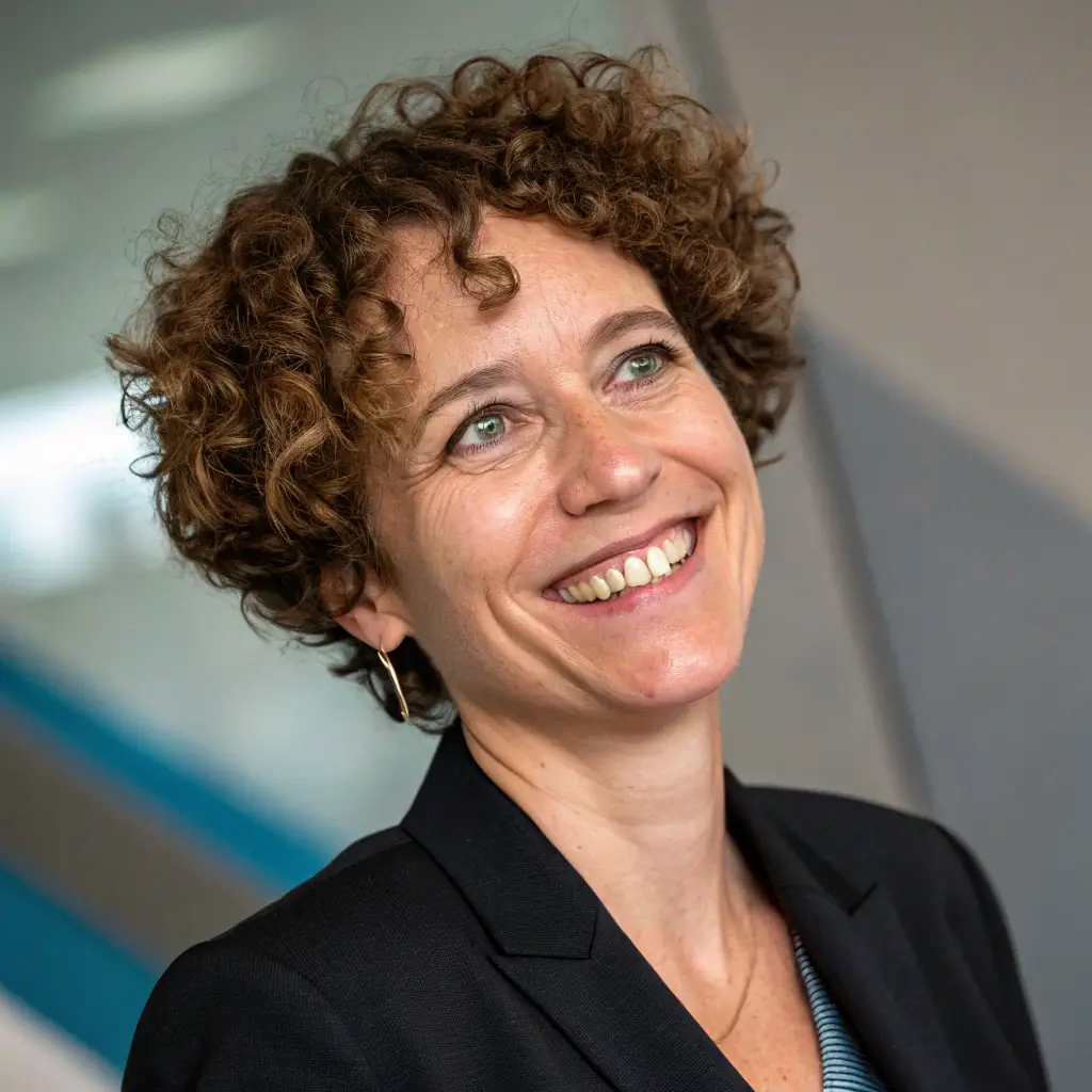 A woman with long black hair, wearing a professional blouse, smiling warmly.