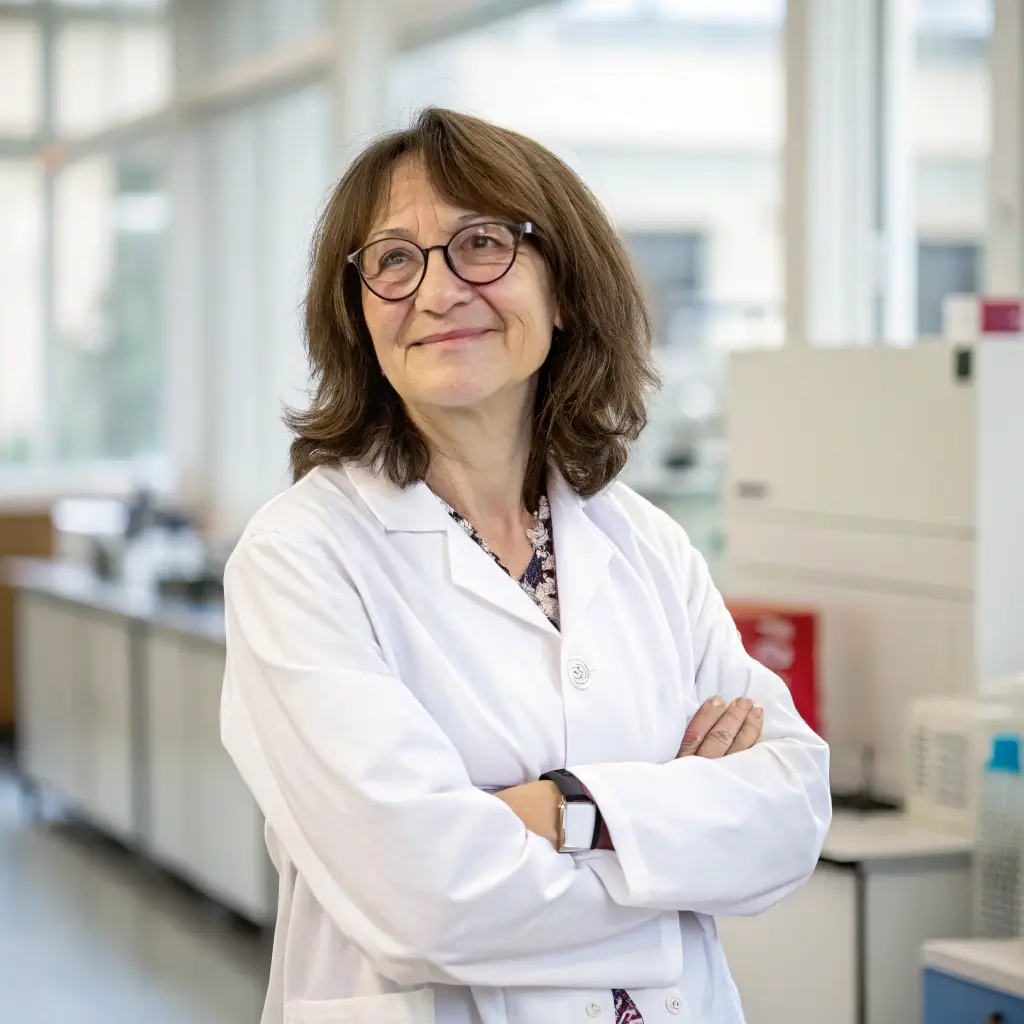 Anya is a woman with short brown hair and glasses, wearing a lab coat and smiling confidently.