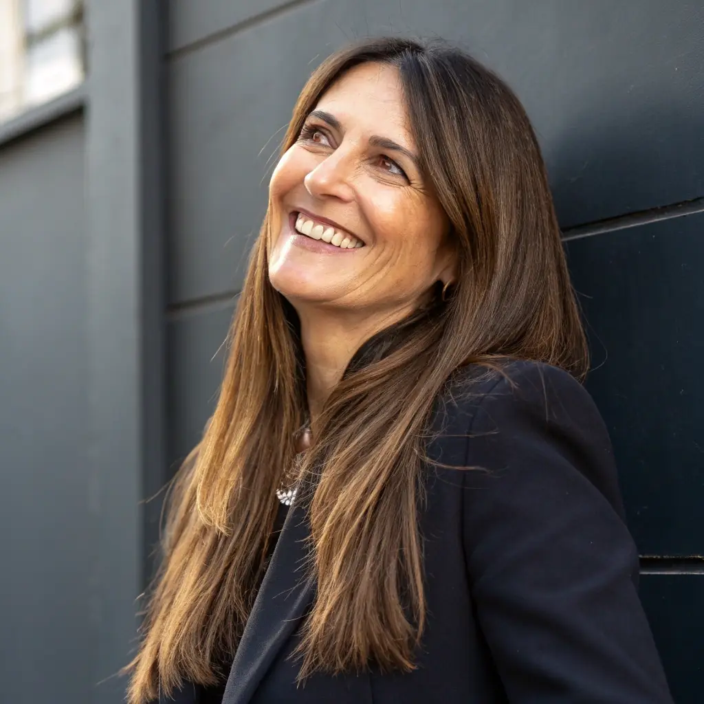 A professional headshot of a smiling woman with short brown hair, wearing a business suit, offset to the right.