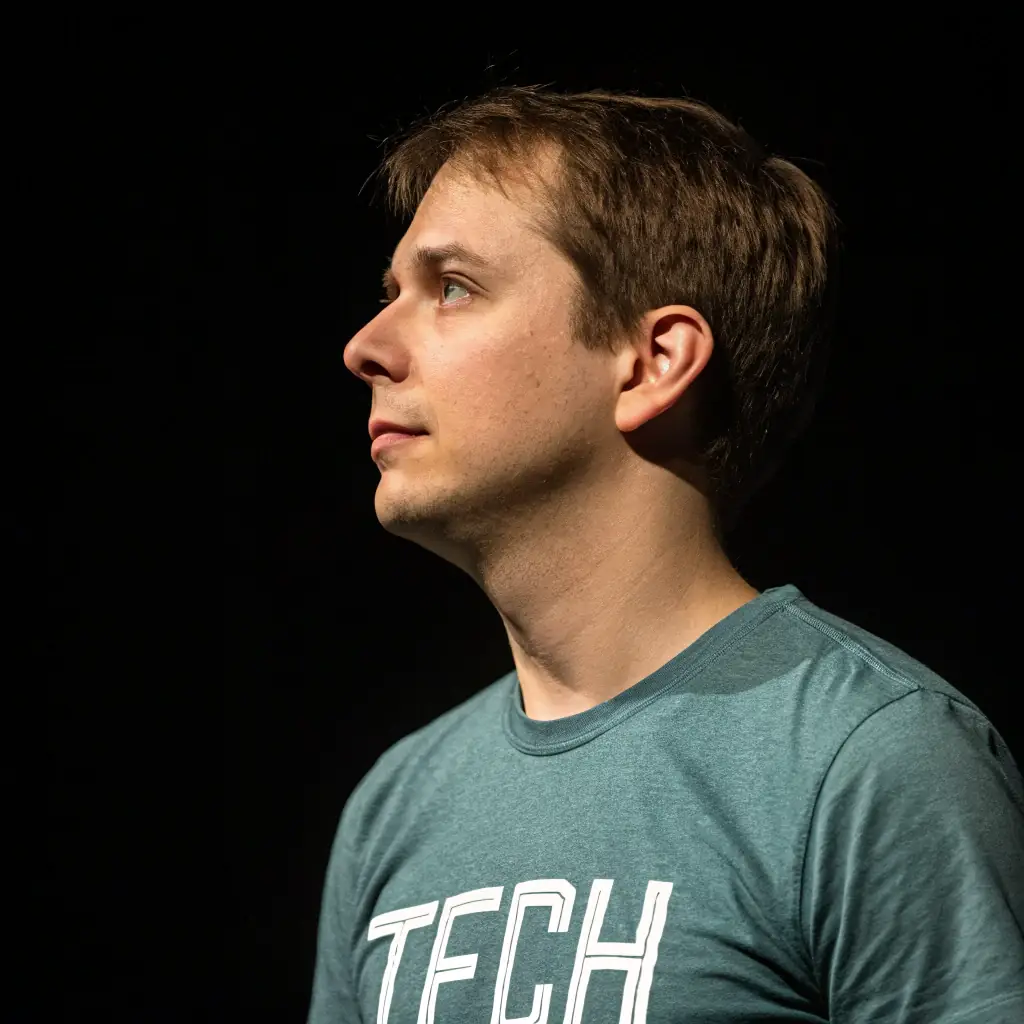 A man with short dark hair, wearing a black t-shirt, looking focused and determined.