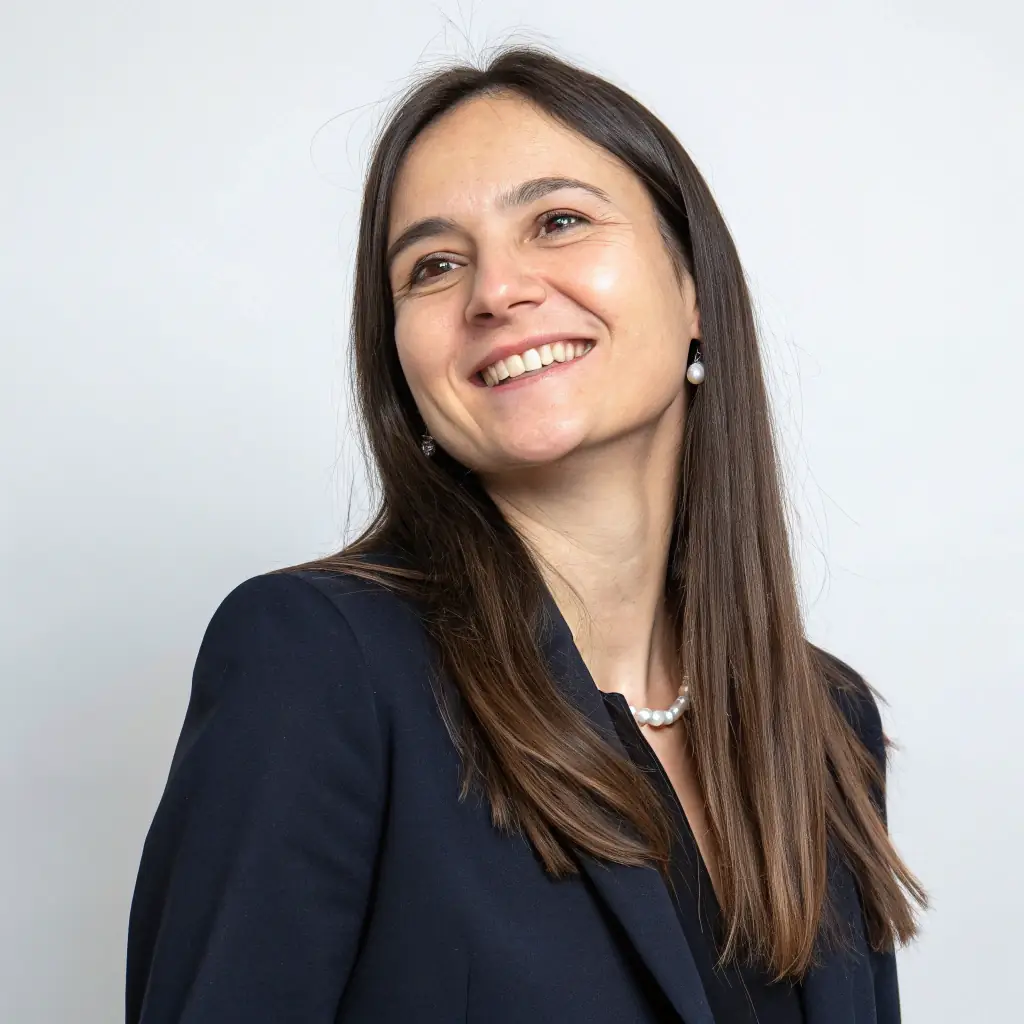 A woman with curly brown hair, wearing a blazer, smiling professionally.